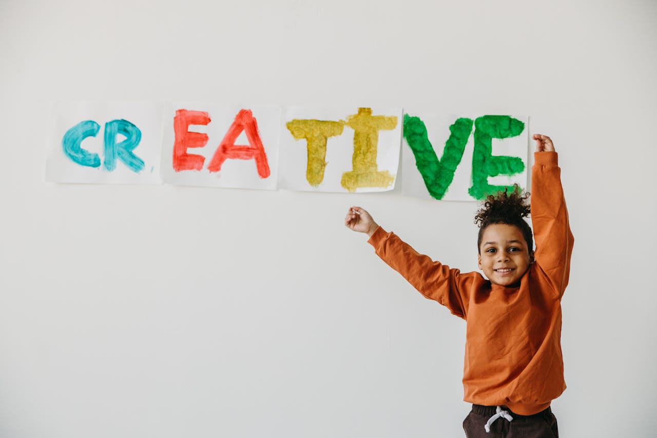 gallery-05 Smiling child with arms up in front of colorful 'creative' art on a white wall.