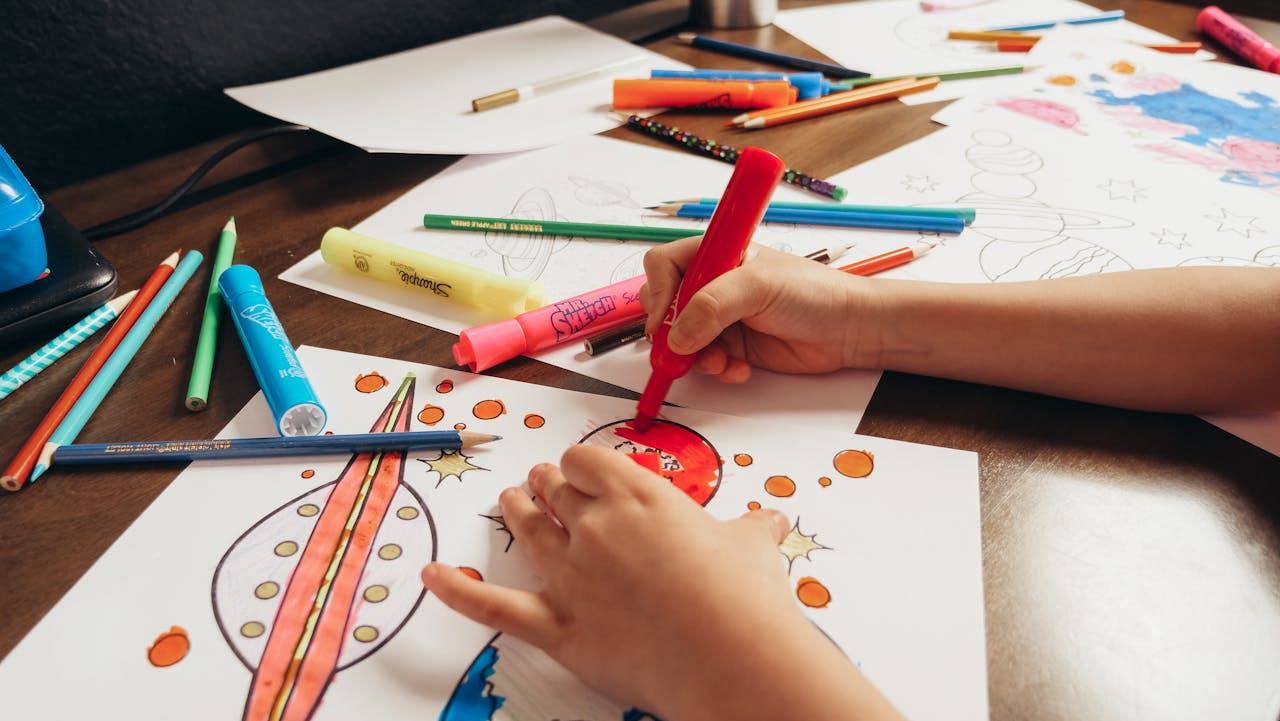 services-01 A child coloring a space-themed picture with colored pencils and markers on a desk.