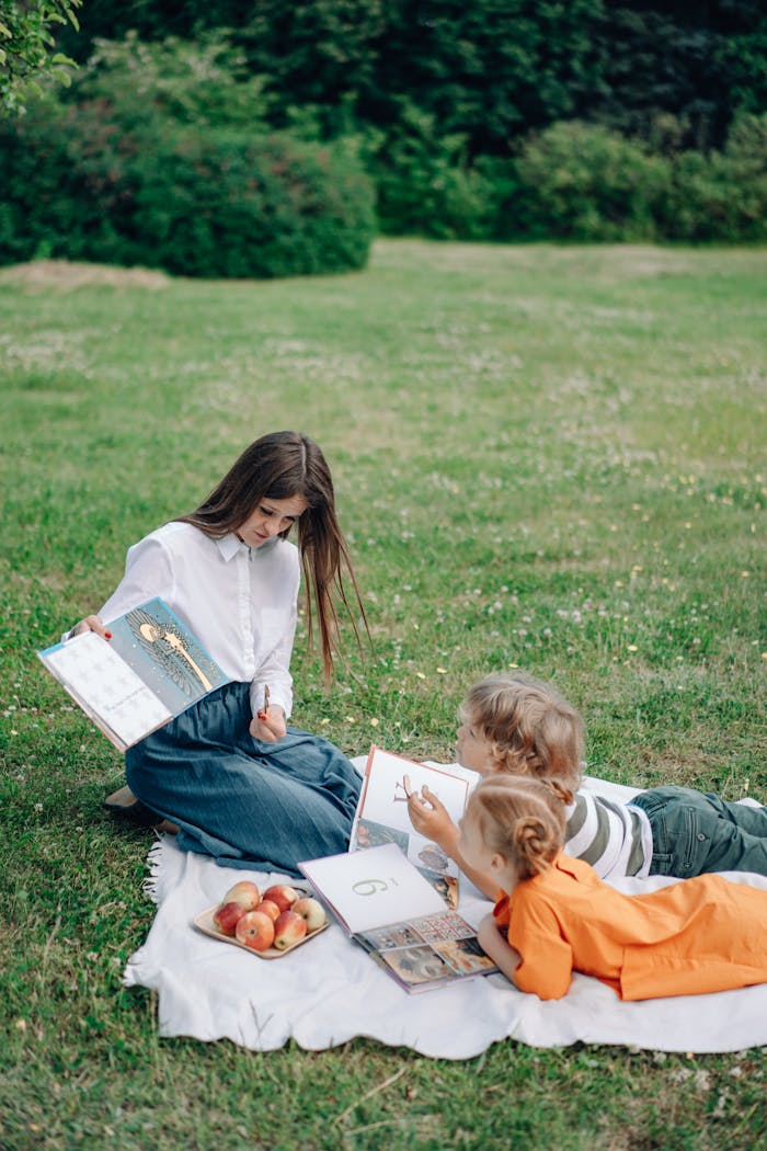 services-02 A woman reads to children on a picnic blanket with apples in a scenic garden.